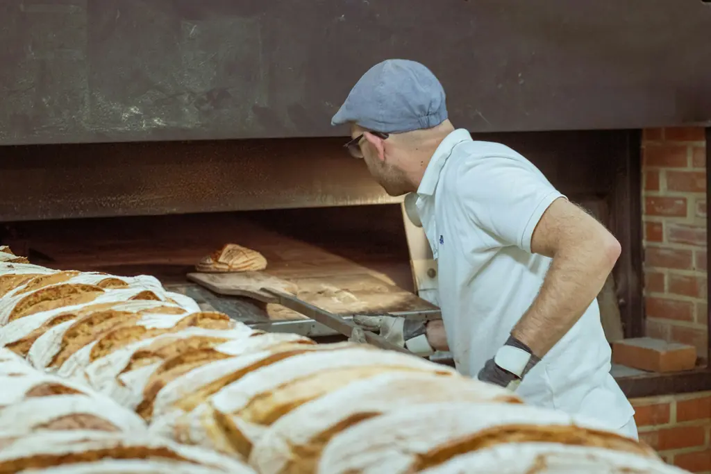 Un panadero trabaja frente al horno junto a panes recién horneados.